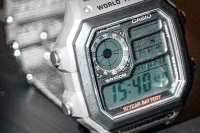 A close-up view of a digital wristwatch with a squared face, displaying time in a large digital format. The watch features multiple functions including a stopwatch and alarm, as indicated by various dials and labels. The watch is marked with the brand name 'CASIO' and a note about a 10-year battery life.