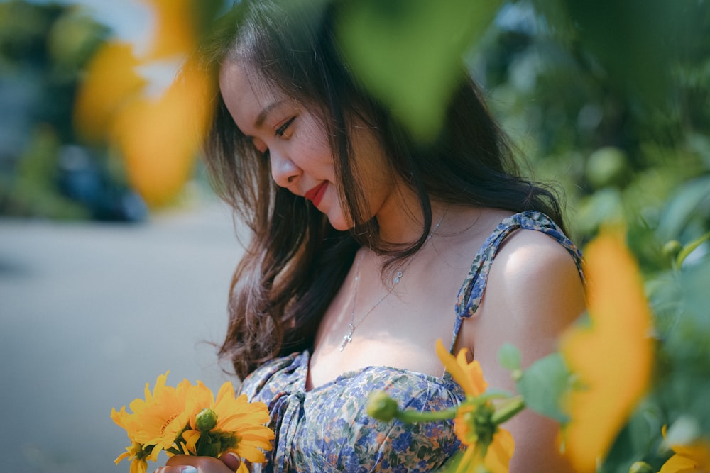 woman in blue and white floral spaghetti strap top holding yellow flower during daytime