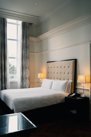 Spacious bedroom with large windows letting in natural light and soft curtains.