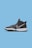 A black athletic sneaker with a white swoosh logo on the side, against a solid blue background. The shoe features a high-top design, black laces, and a white outsole with textured black grip.