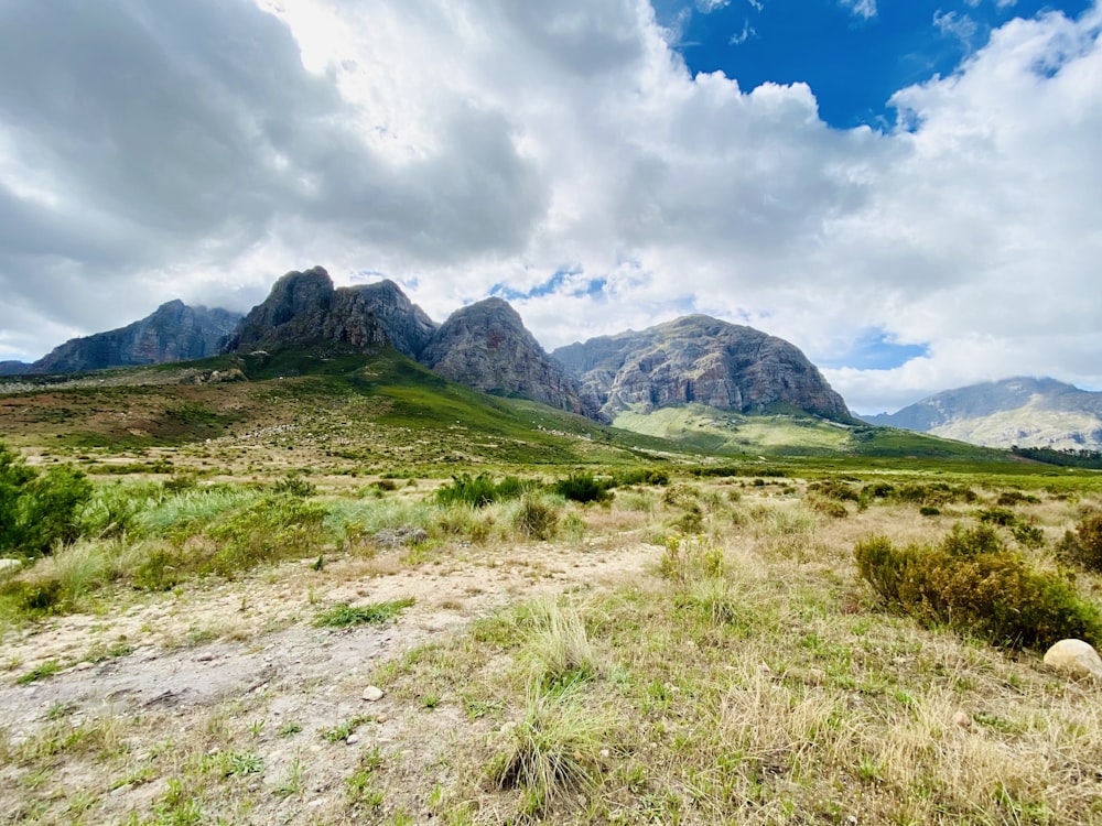 green grass field near mountain under white clouds and blue sky during daytime