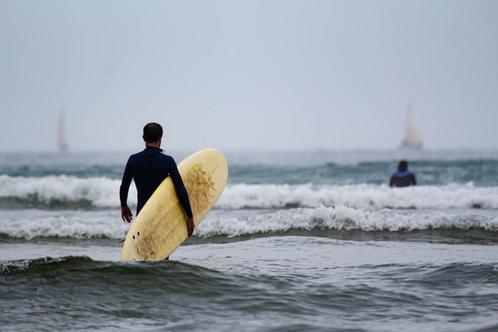 man in black wetsuit carrying white surfboard on sea during daytime