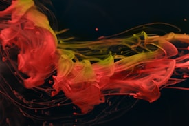 Vivid swirls of red and yellow ink merge and flow gracefully against a dark background, creating a dynamic and abstract composition. The colors blend smoothly, forming intricate patterns with a sense of fluid motion.