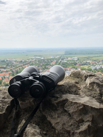 Close-up of a rugged, black binocular resting on a rocky ledge with misty mountains in the background.