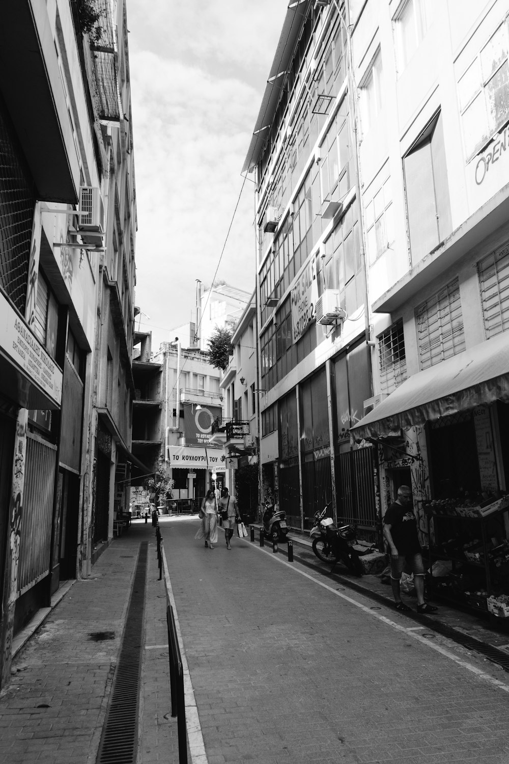 grayscale photo of people walking on street in between buildings