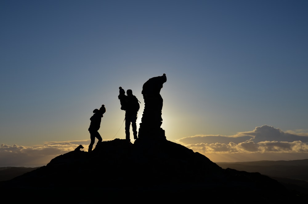 silhouette of 2 men standing on rock formation during sunset