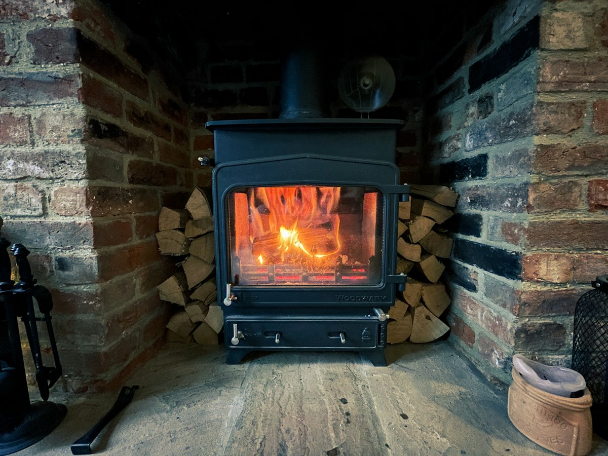 Black wood-burning stove in front of a brick wall with a fire burning
