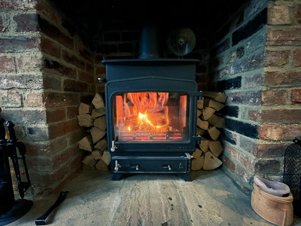 Black wood-burning stove in front of a brick wall with a fire burning