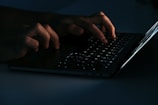 Hands typing on laptop keyboard in bright workspace.