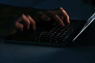 Close-up of hands typing on a laptop keyboard with a dark-themed website on the screen.