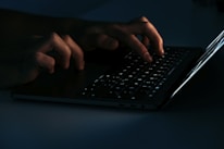 Close-up of hands typing on a laptop keyboard in a bright workspace.