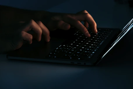 Close-up of hands typing on a laptop keyboard with green and black ambient lighting.