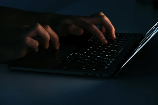 Close-up of hands typing on a laptop keyboard with a dark-themed website on the screen.