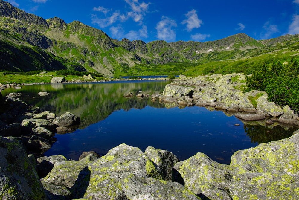 green and gray mountain beside lake under blue sky during daytime