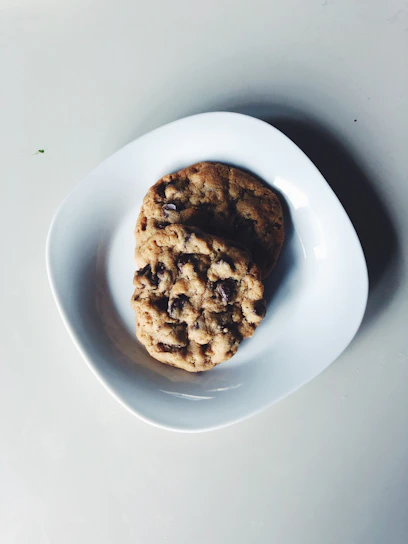 Close-up of a freshly baked American cookie with golden edges and chocolate chunks on a minimalist white plate.