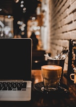 Cozy coffee shop counter with a laptop and a steaming cup of oat milk latte.