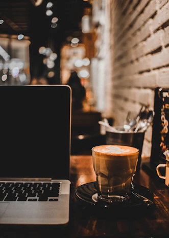 A cozy coffee shop corner with warm lighting and a laptop open beside a latte.
