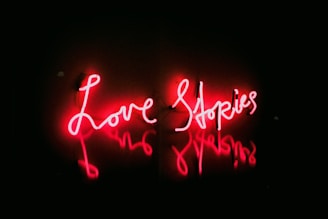 Neon text in bright red reads 'Love Stories' against a dark background, creating a glowing effect on the surrounding surface.