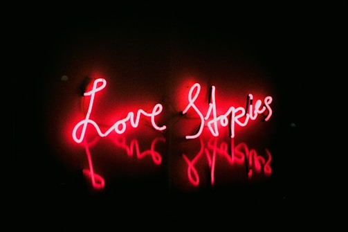 Neon text in bright red reads 'Love Stories' against a dark background, creating a glowing effect on the surrounding surface.