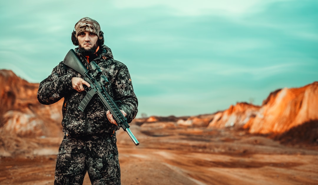 man in black and gray camouflage jacket holding rifle