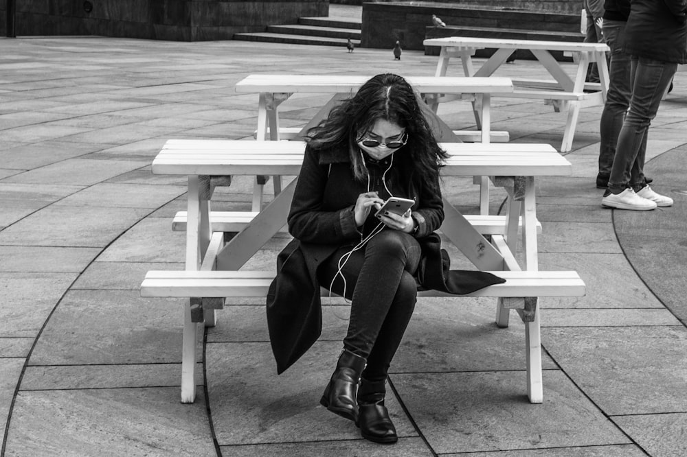 woman in black leather jacket sitting on white wooden bench