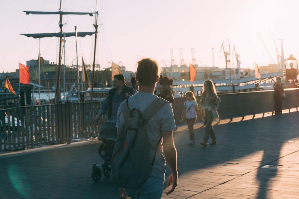 man in blue shirt and black backpack walking on sidewalk during daytime