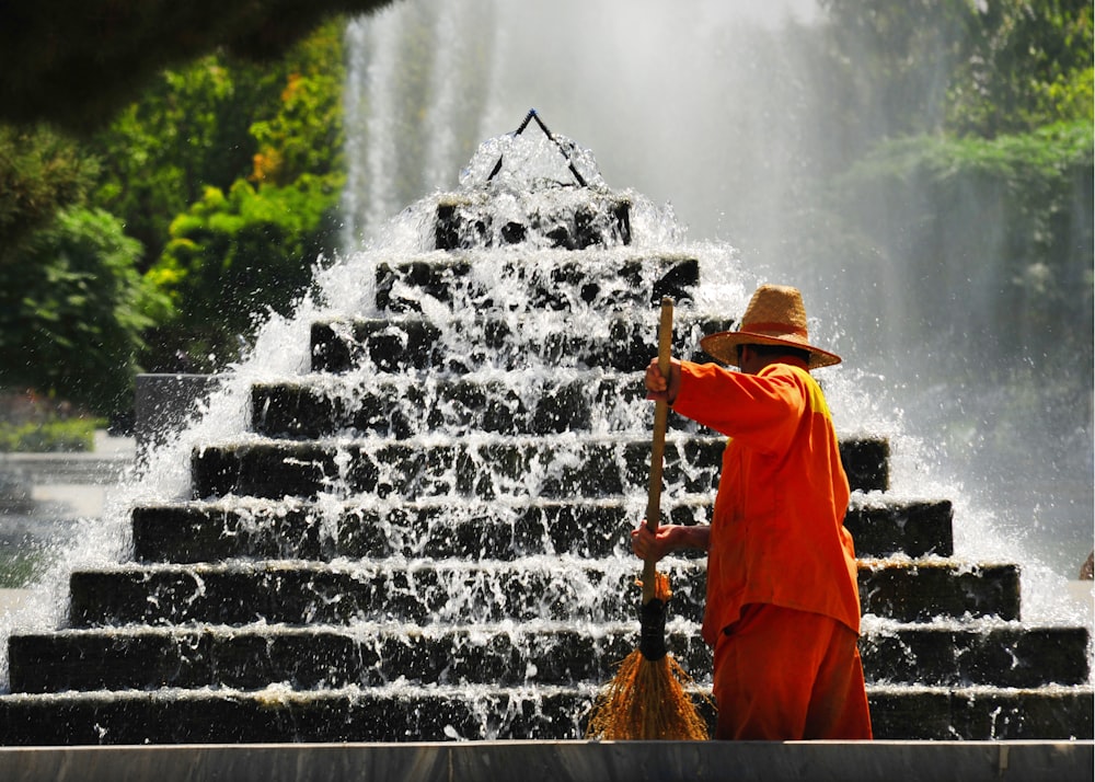 man in orange robe standing on water fountain during daytime