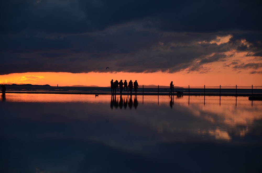 silhouette of people standing on dock during sunset