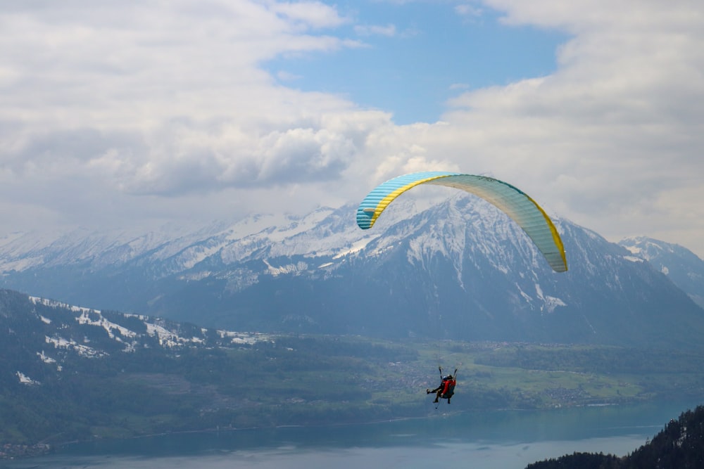 Persona in giacca nera e pantaloni blu che cavalca sul paracadute giallo sopra le montagne durante il giorno