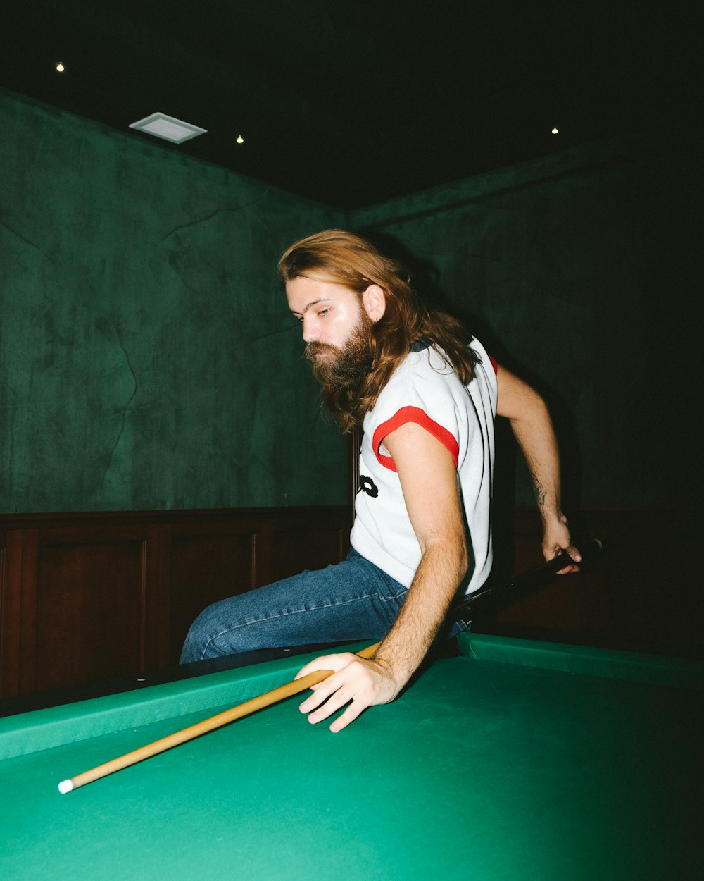 woman in white and red jersey shirt and blue denim jeans sitting on billiard table