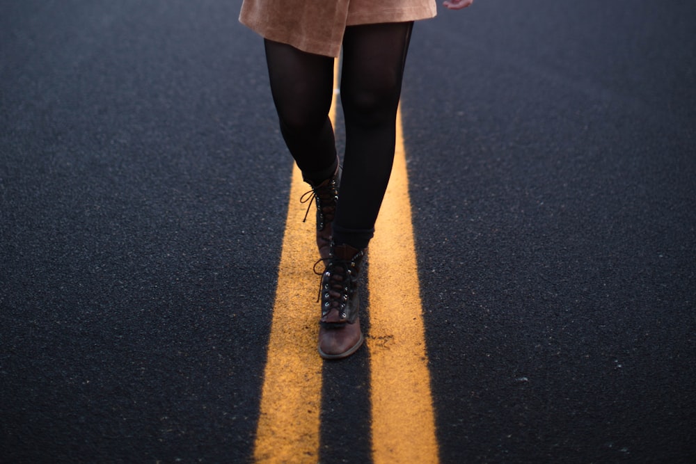 person in black leather boots standing on black asphalt road