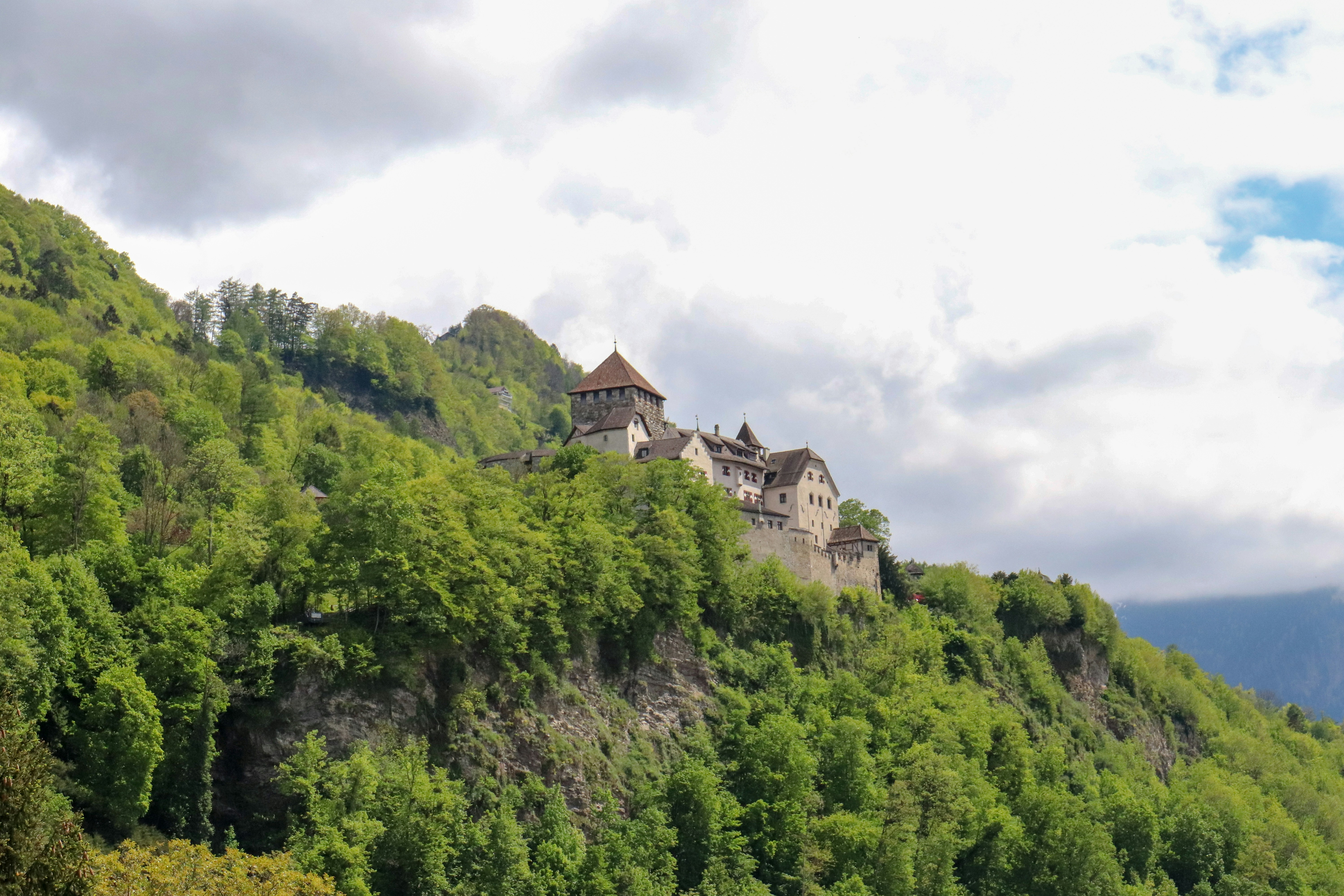 white and brown concrete building on top of green mountain liechtenstein teams background