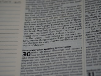 A close-up view of a page from a book with text in English. The page contains religious or biblical text, featuring bold and italicized headings along with sequential verse numbers.