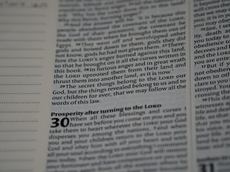 A close-up view of a page from a book with text in English. The page contains religious or biblical text, featuring bold and italicized headings along with sequential verse numbers.