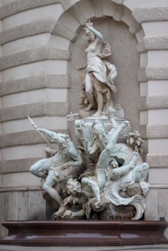 A marble sculpture depicting a mythological scene with a prominently positioned female figure standing over several other figures and sea creatures. The figures are detailed with flowing garments and dynamic poses, seemingly engaged in a dramatic interaction. The background is an ornate architectural niche with textured stonework.