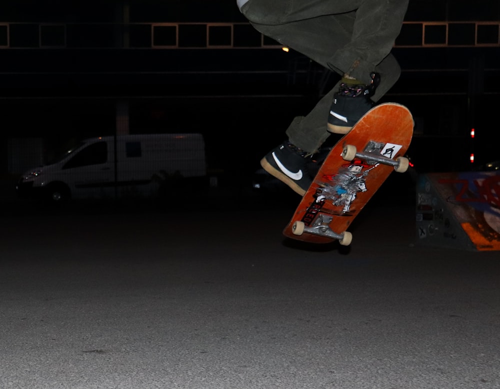 Personne en pantalon gris et baskets noires et oranges chevauchant une planche à roulettes orange