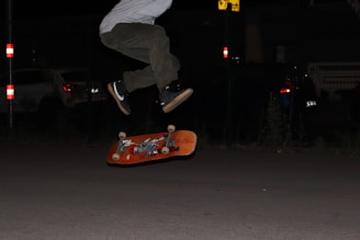 person in white pants and black shoes standing on orange skateboard during night time