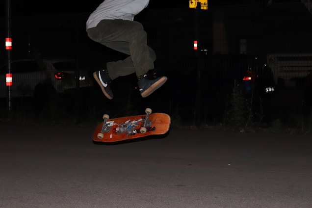person in white pants and black shoes standing on orange skateboard during night time