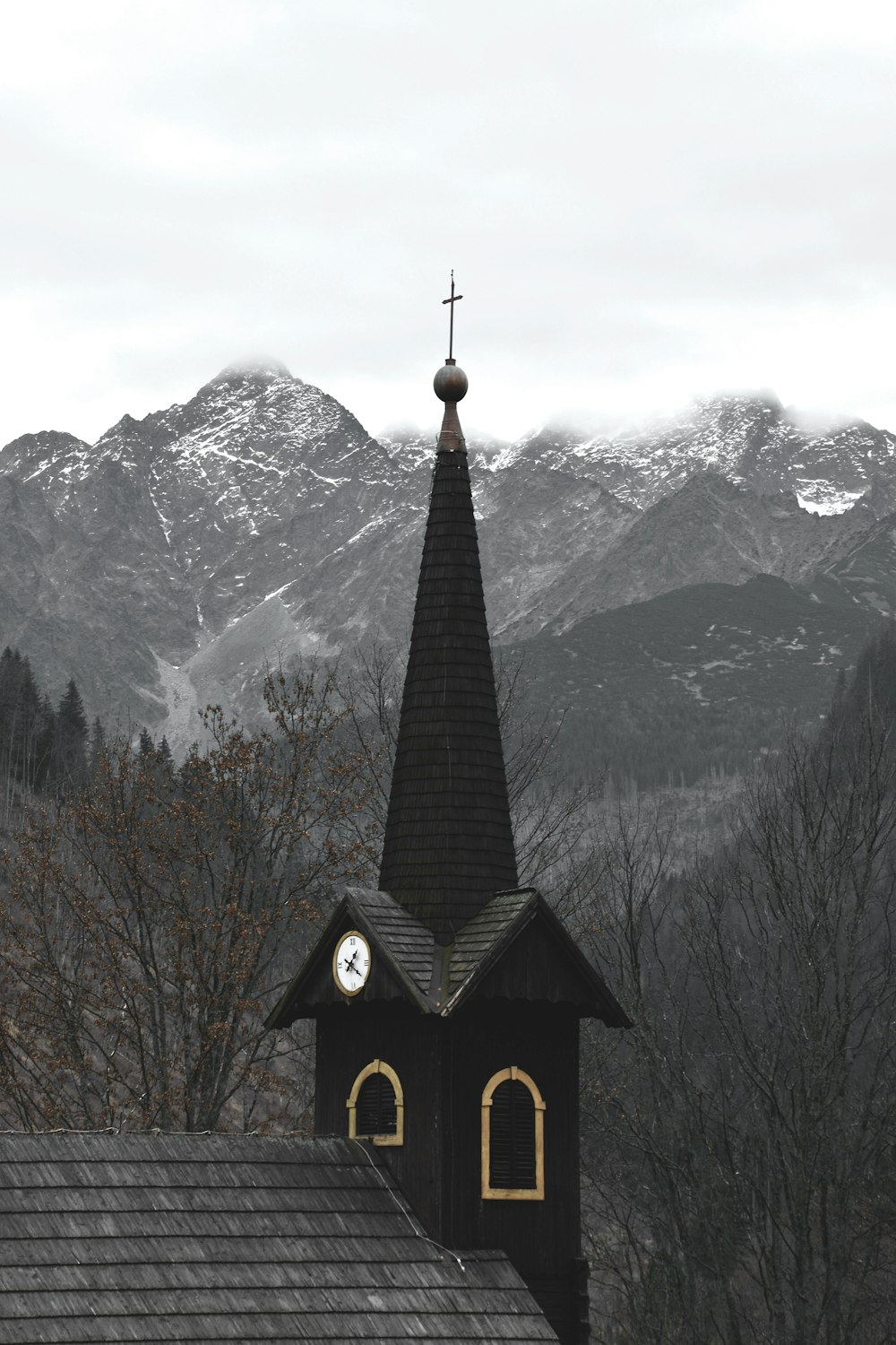 Iglesia en blanco y negro cerca de árboles desnudos marrones y montañas cubiertas de nieve durante el día