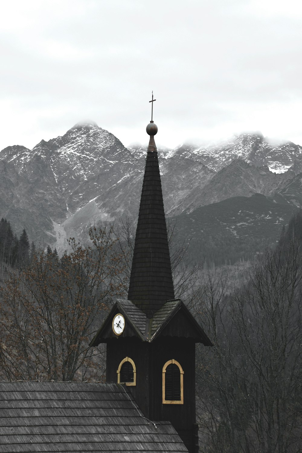 black and white church near brown bare trees and snow covered mountain during daytime