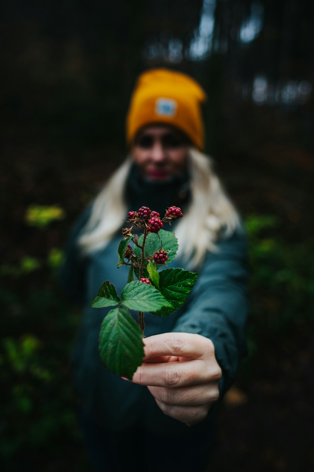 woman in green jacket holding red and yellow flower