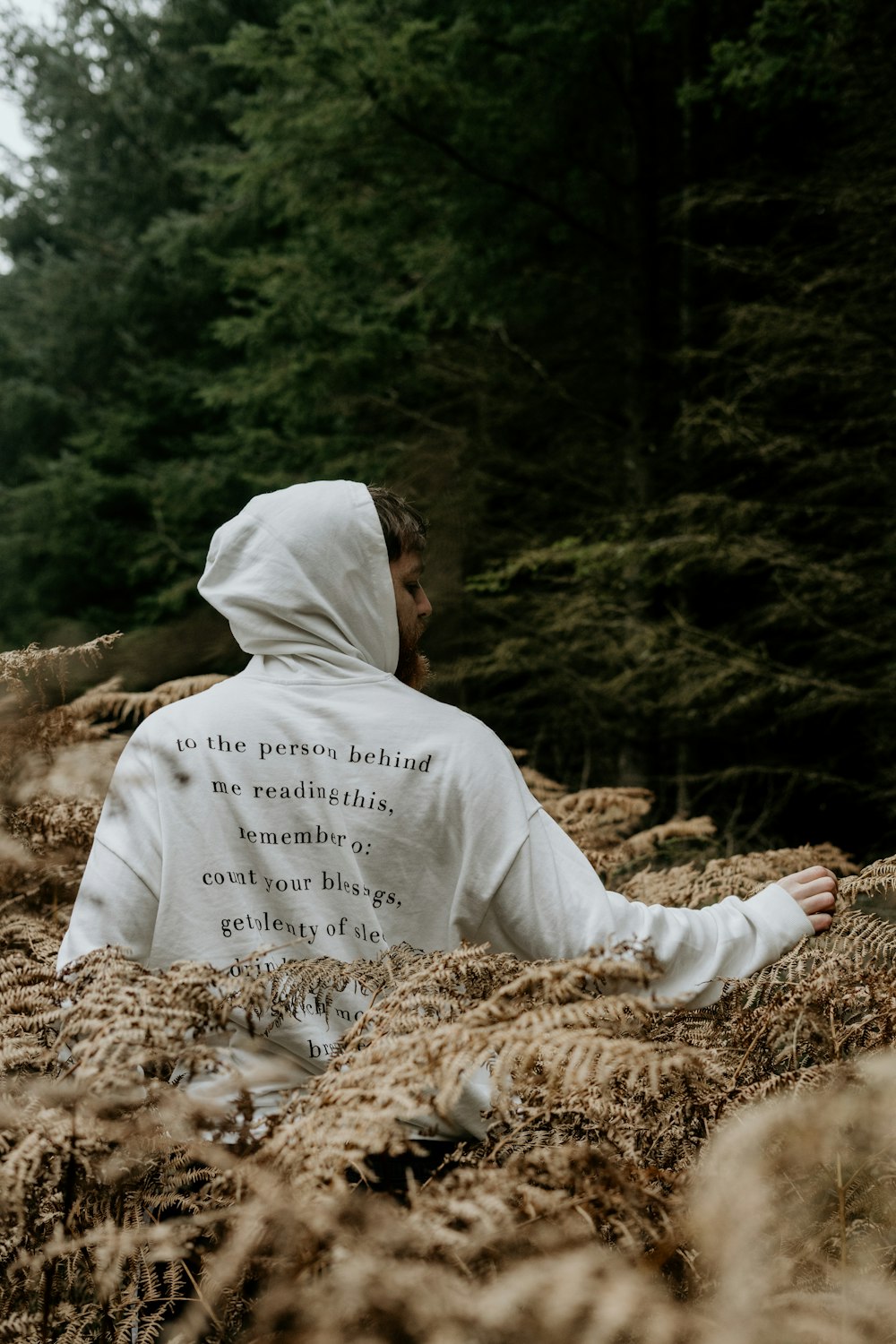 person in white hoodie sitting on brown dried leaves during daytime