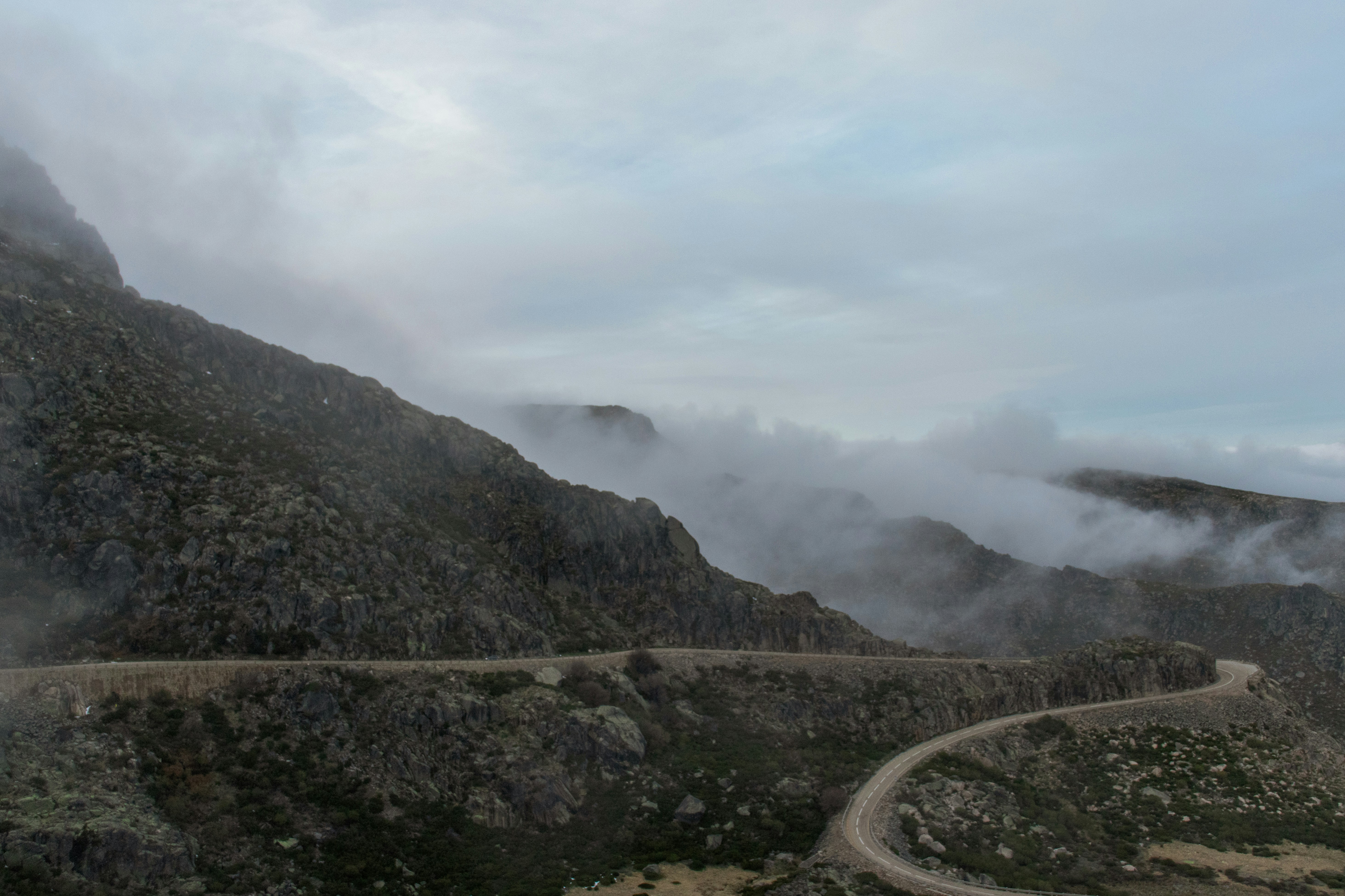 gray concrete road near mountain under white clouds during daytime
