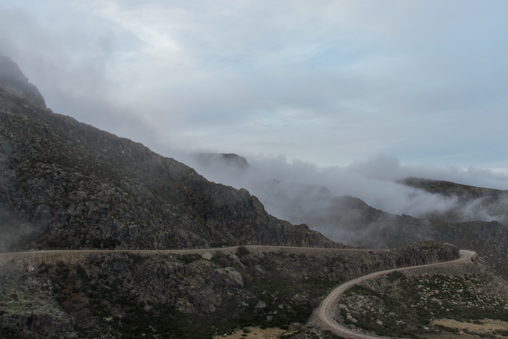 gray concrete road near mountain under white clouds during daytime