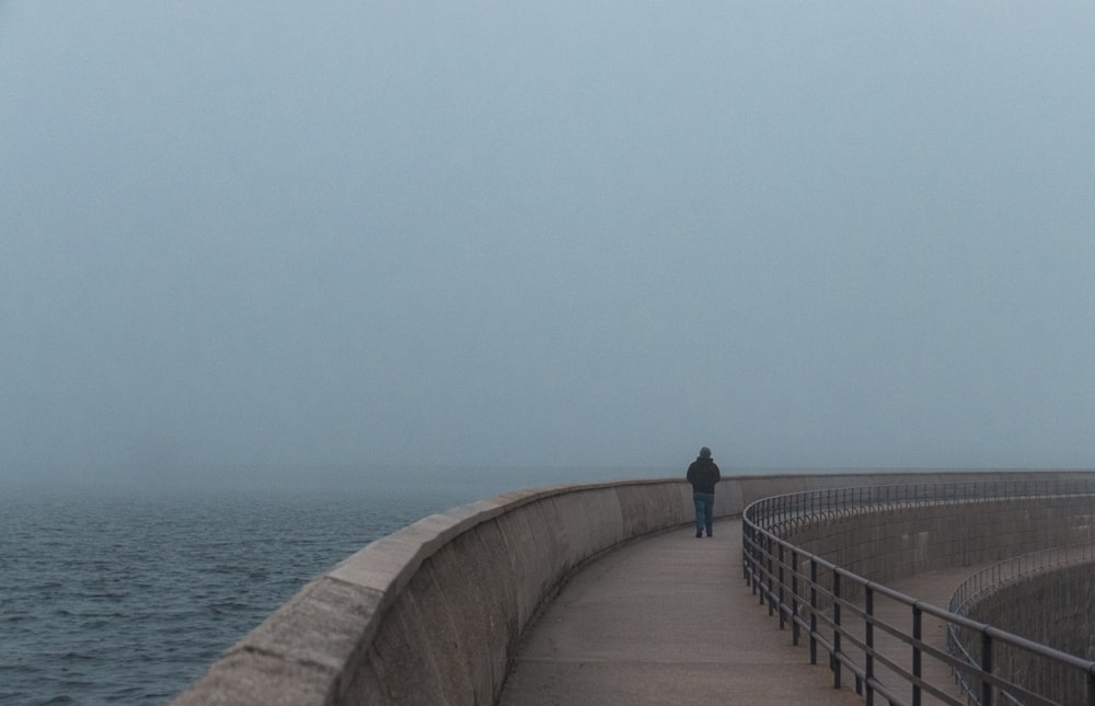personne en veste noire debout sur un pont en béton gris pendant la journée