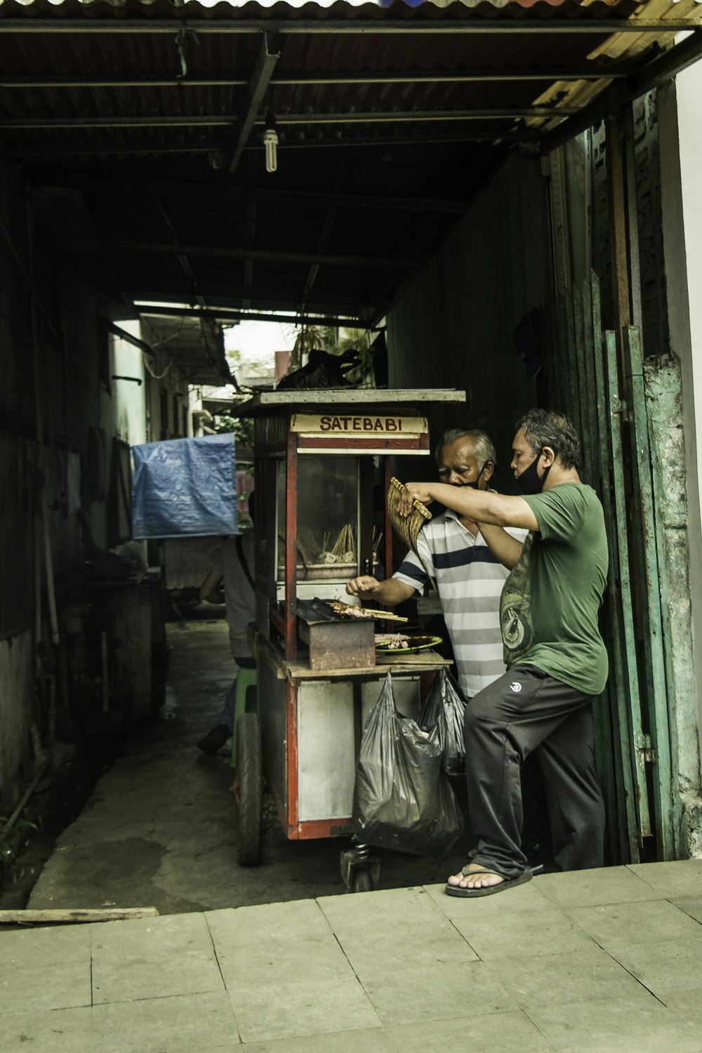 man in green and white striped polo shirt sitting on blue and white food cart