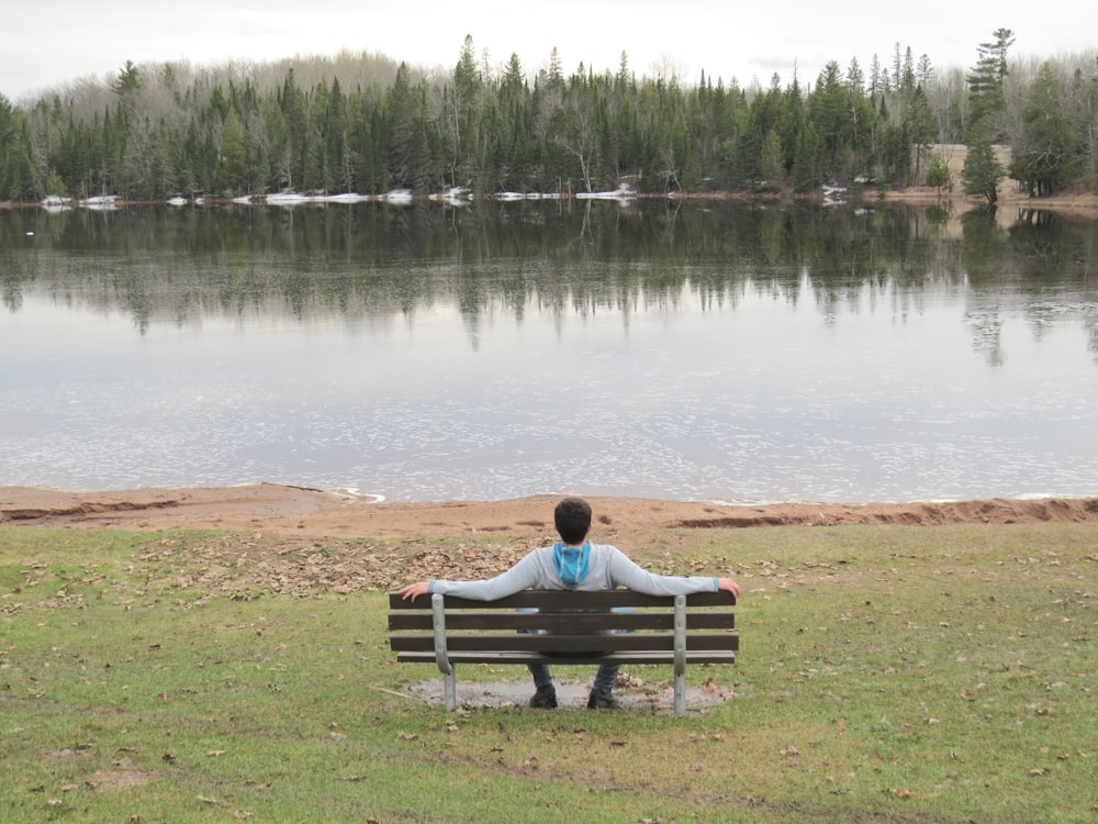 woman sitting on bench near lake during daytime