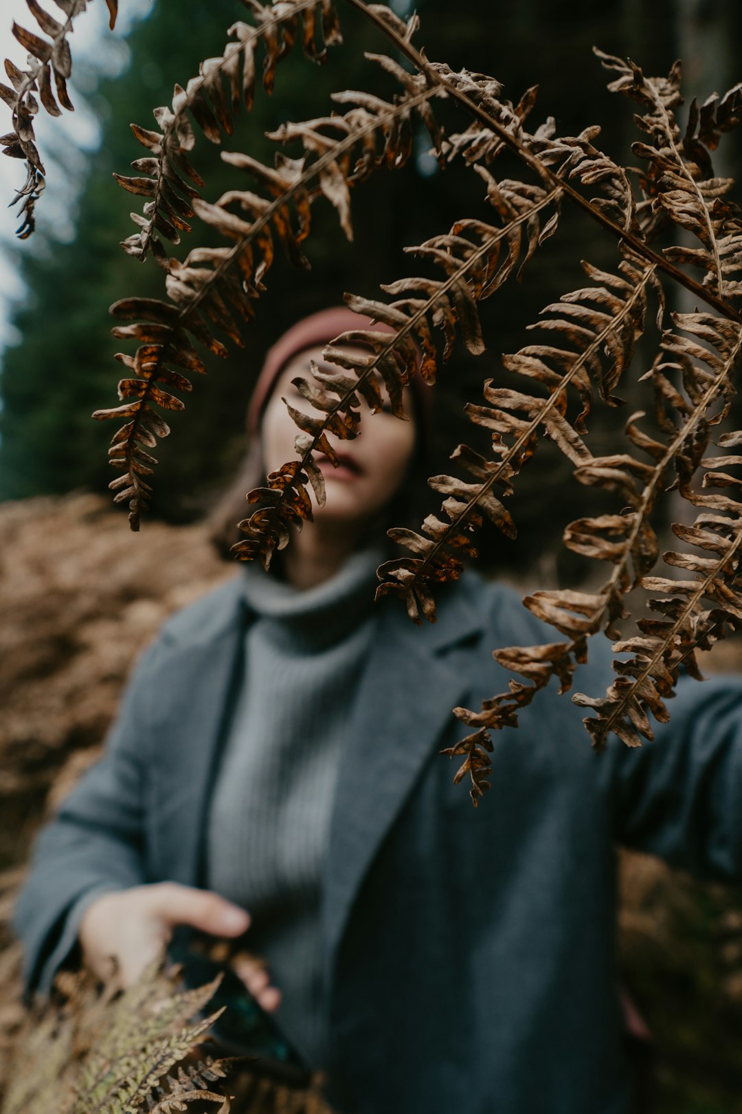 person in gray sweater standing near brown dried leaves during daytime