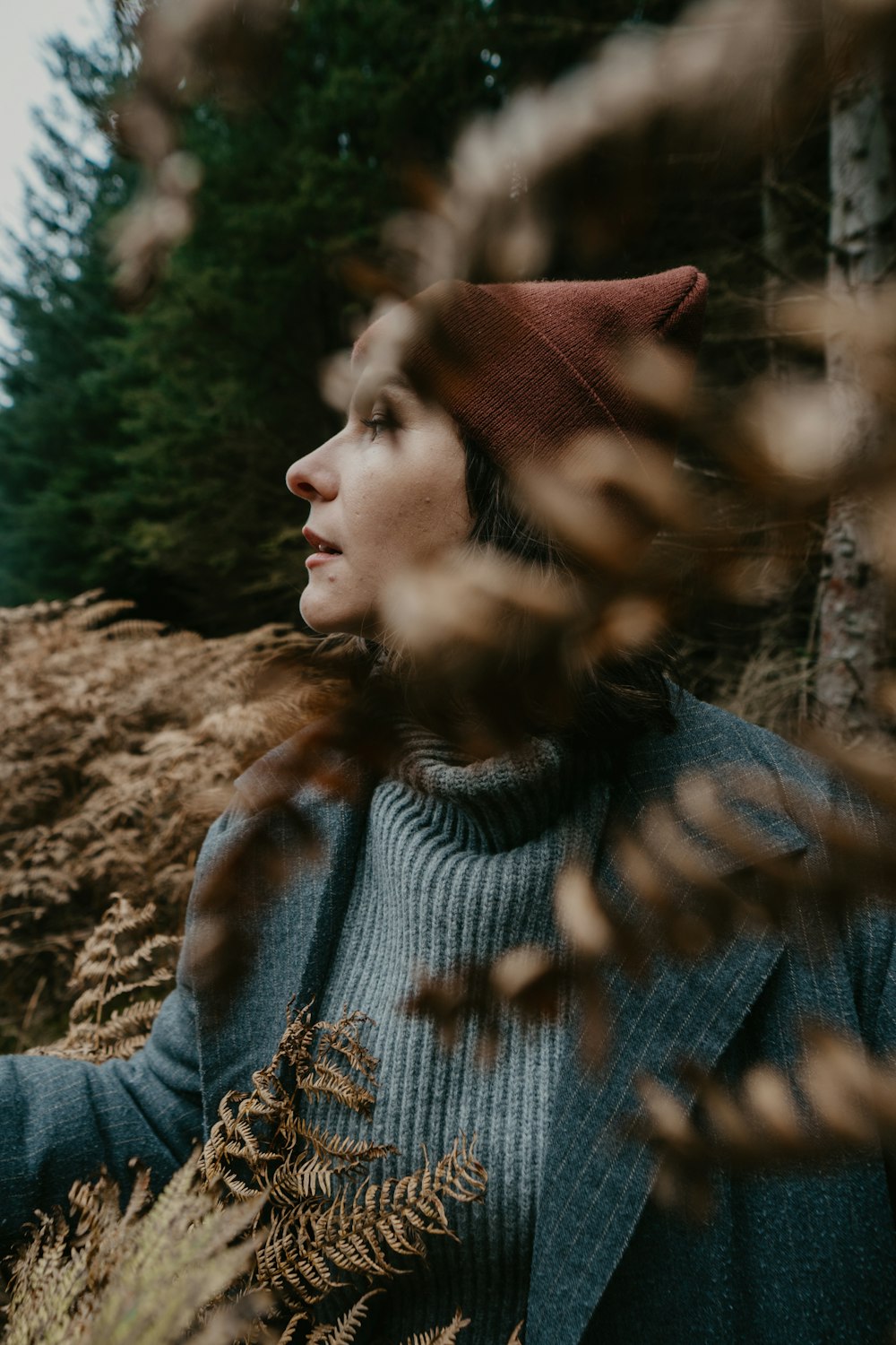 woman in gray sweater standing near green trees during daytime