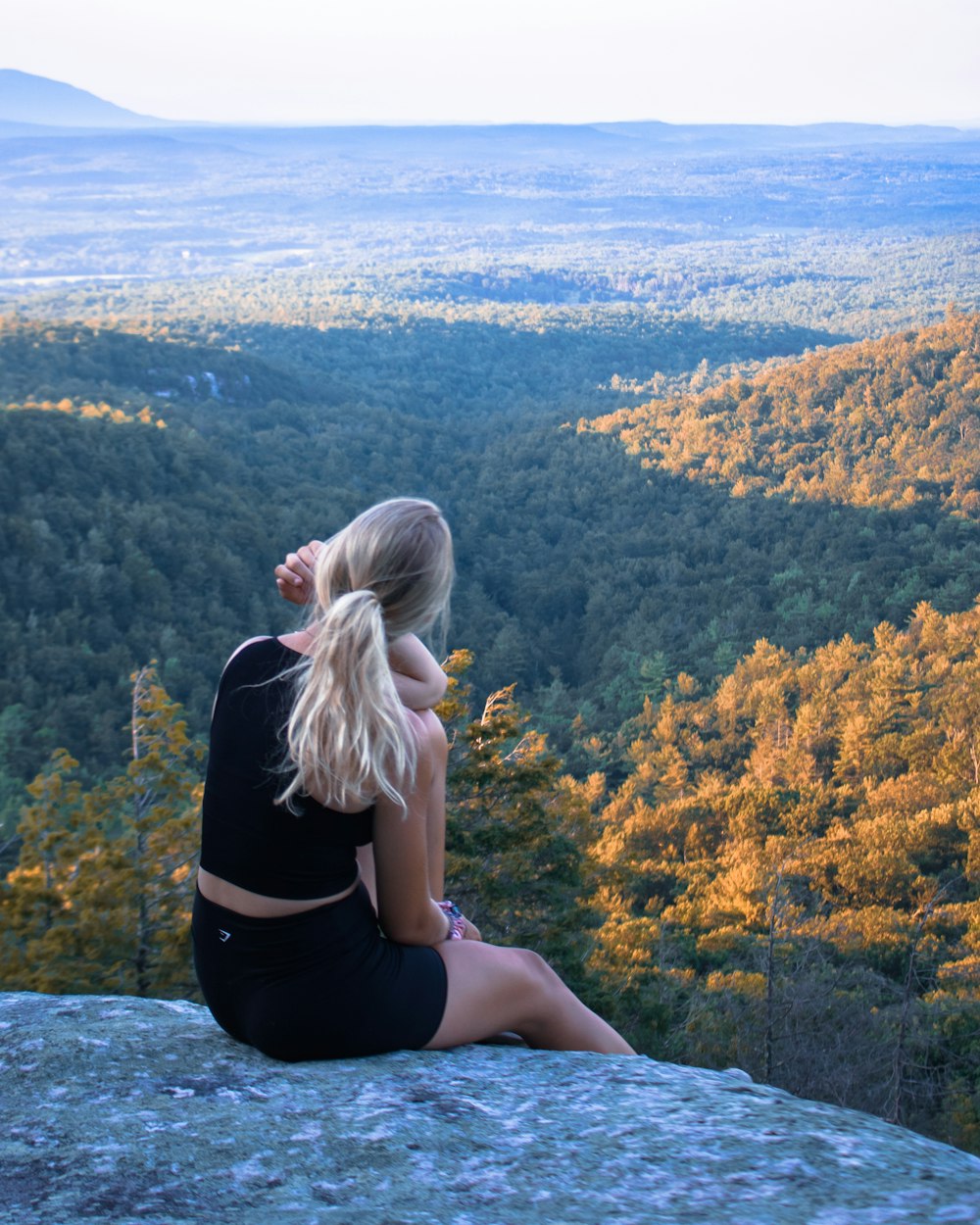 woman in black dress sitting on rock looking at the sea during daytime